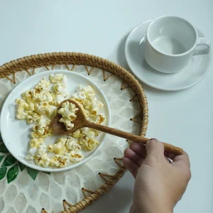 Hand holding a heart-shaped wooden spoon with popcorn