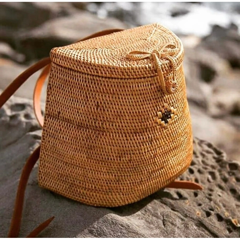 Natural woven backpack with a dark decorative motif resting on rocks