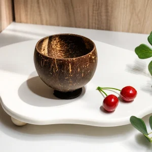 Handmade coconut shell cup on a white tabletop tray with cherries