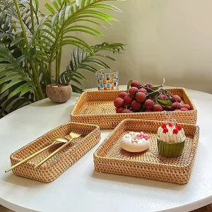 Three handwoven rattan trays displaying fruit, cakes and cutlery on a round table